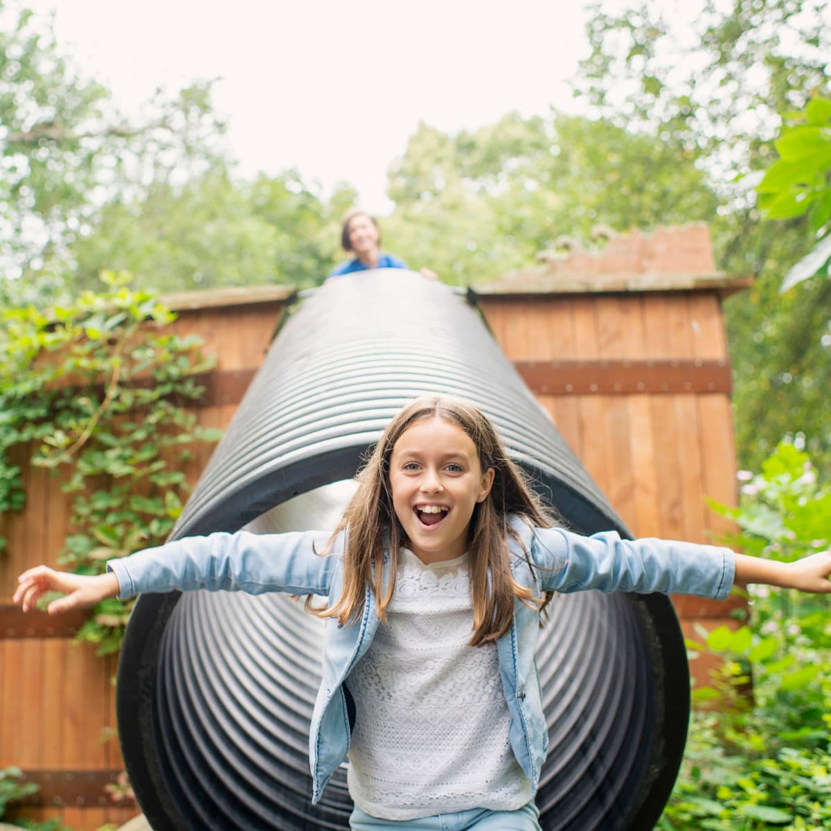 A little girl standing in front of a metal cylinder in a garden.