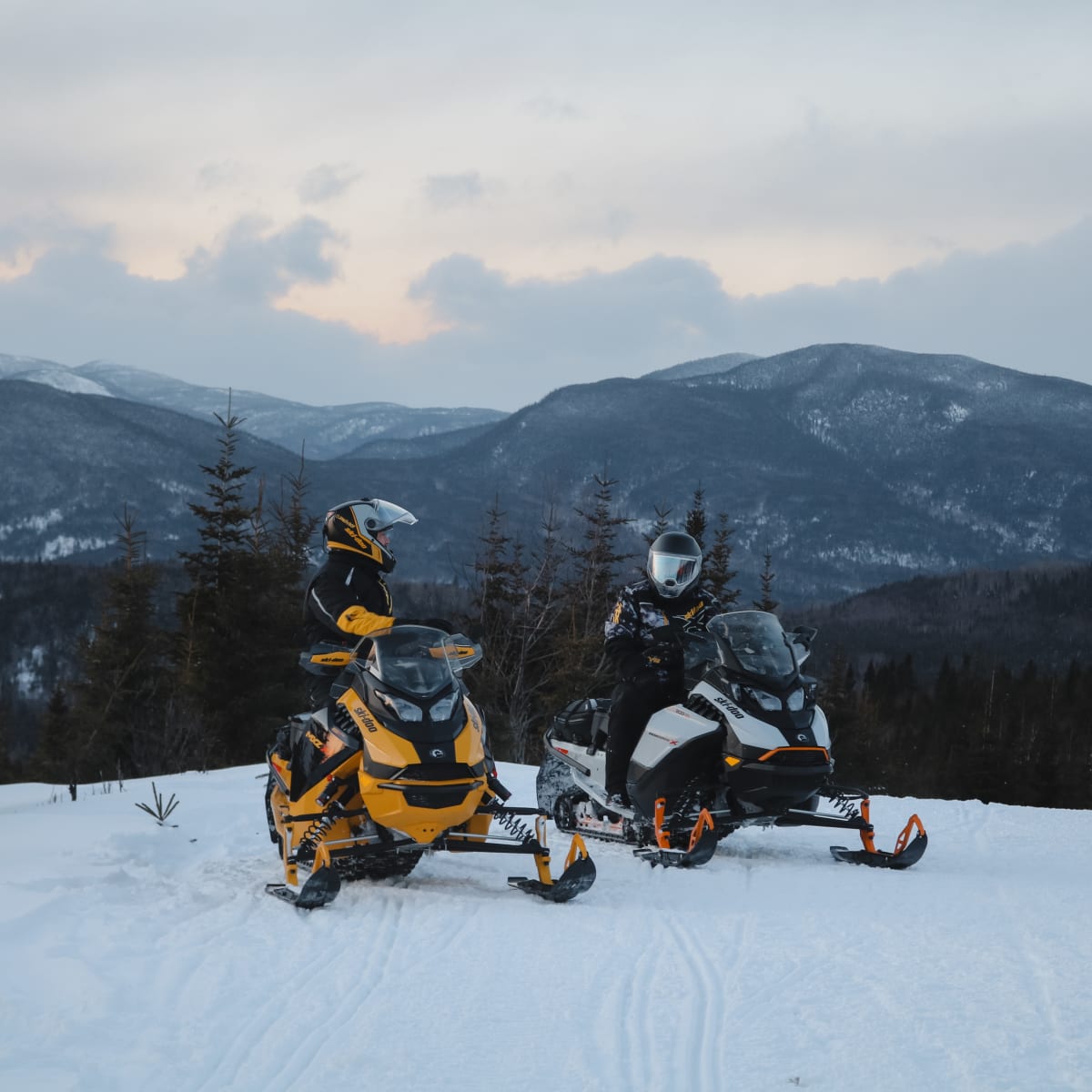 Deux motoneigistes sur un sentier, avec montagnes en arrière-plan.