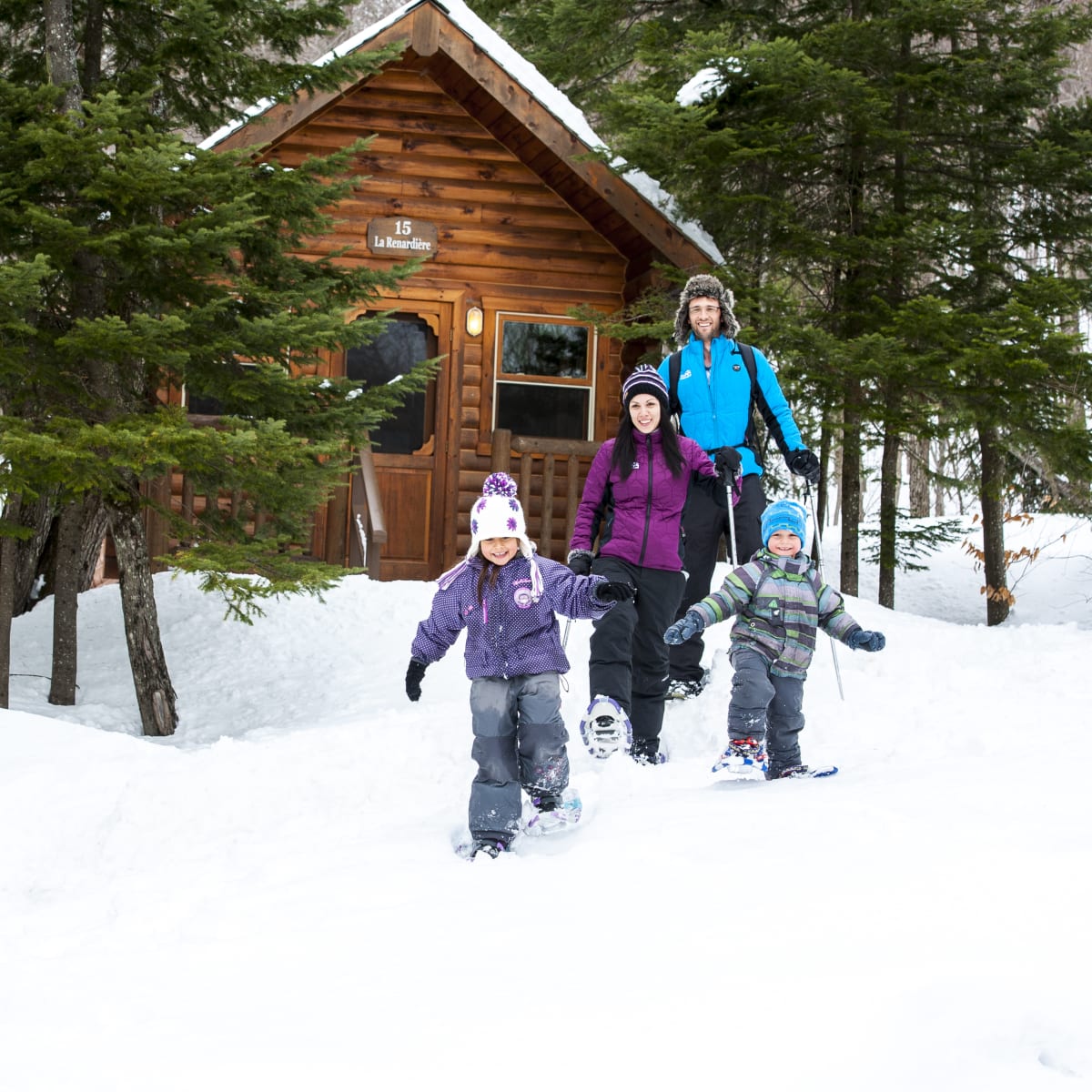 Une famille en raquette à côté d'un chalet au Sommet Morin Heights.