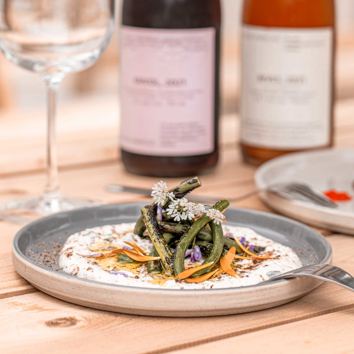 A close-up of a carefully arranged plate, with a wine glass and two bottles of wine in the background.