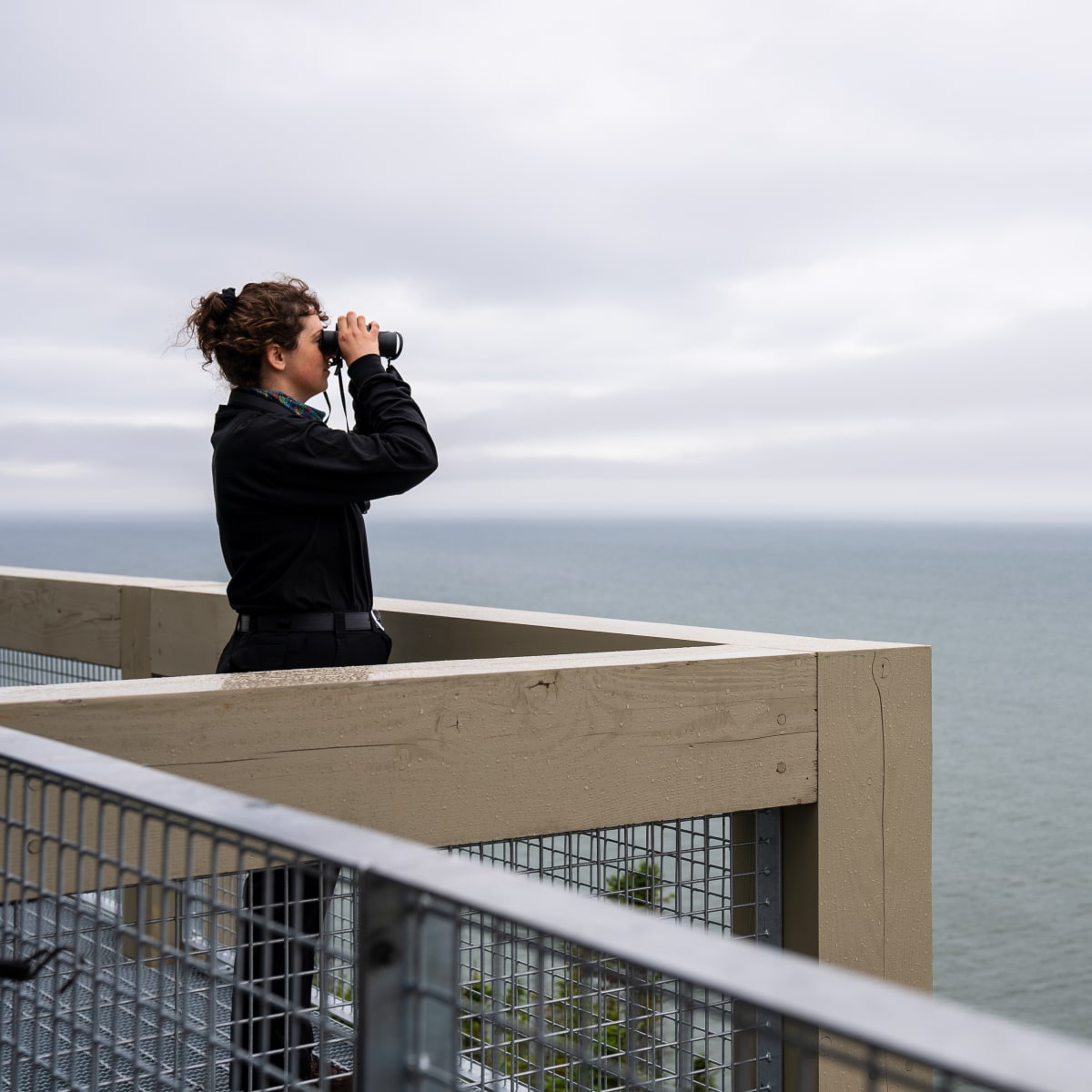Femme, jumelles à la main, en train d'observer l'horizon au site d’observation Putep’t-awt