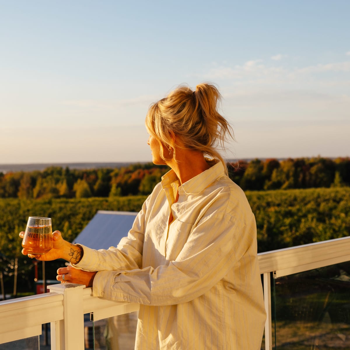 A woman holding a glass and looking out at the horizon from a patio. 