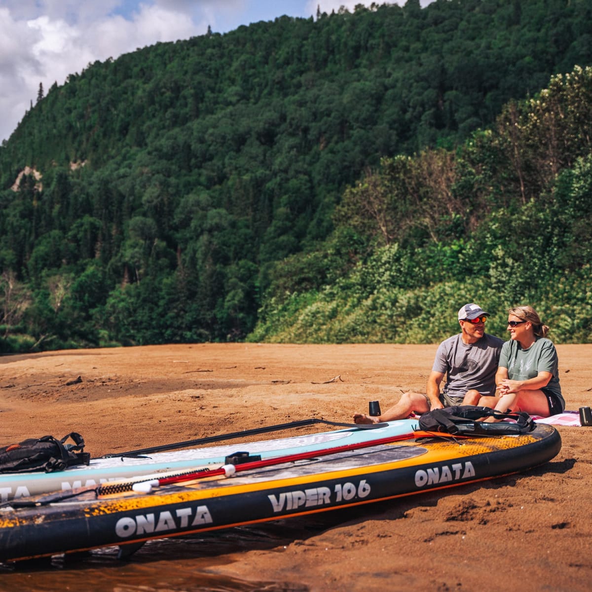 A couple sitting on the shore with their stand-up paddleboards.