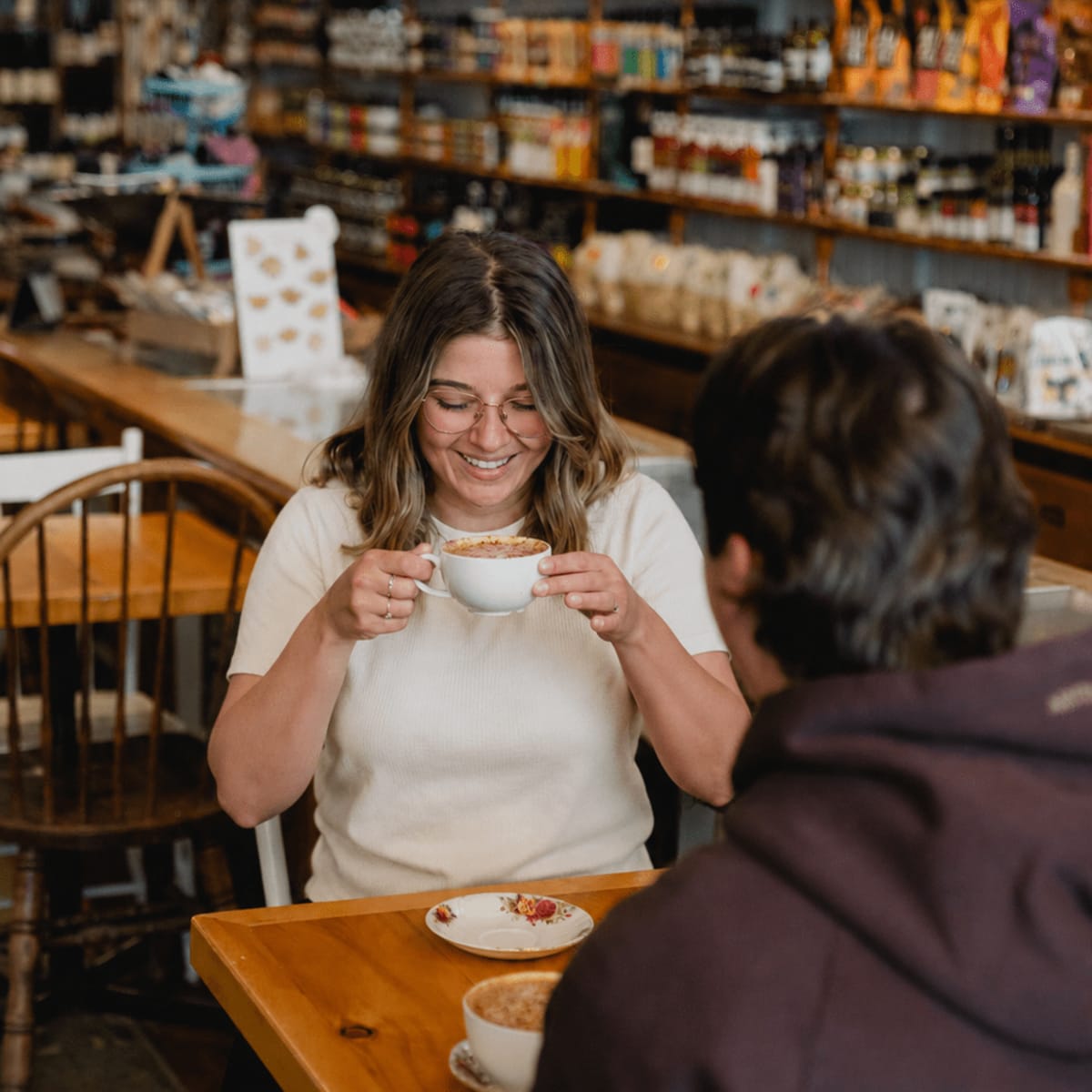 A couple sitting at a table at the Aux cinq sœurs coffee shop; the woman is holding a cup.
