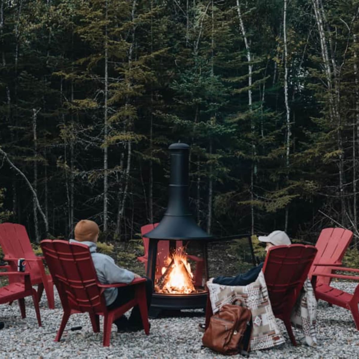 People sitting on red Adirondack chairs around an outdoor fire pit.