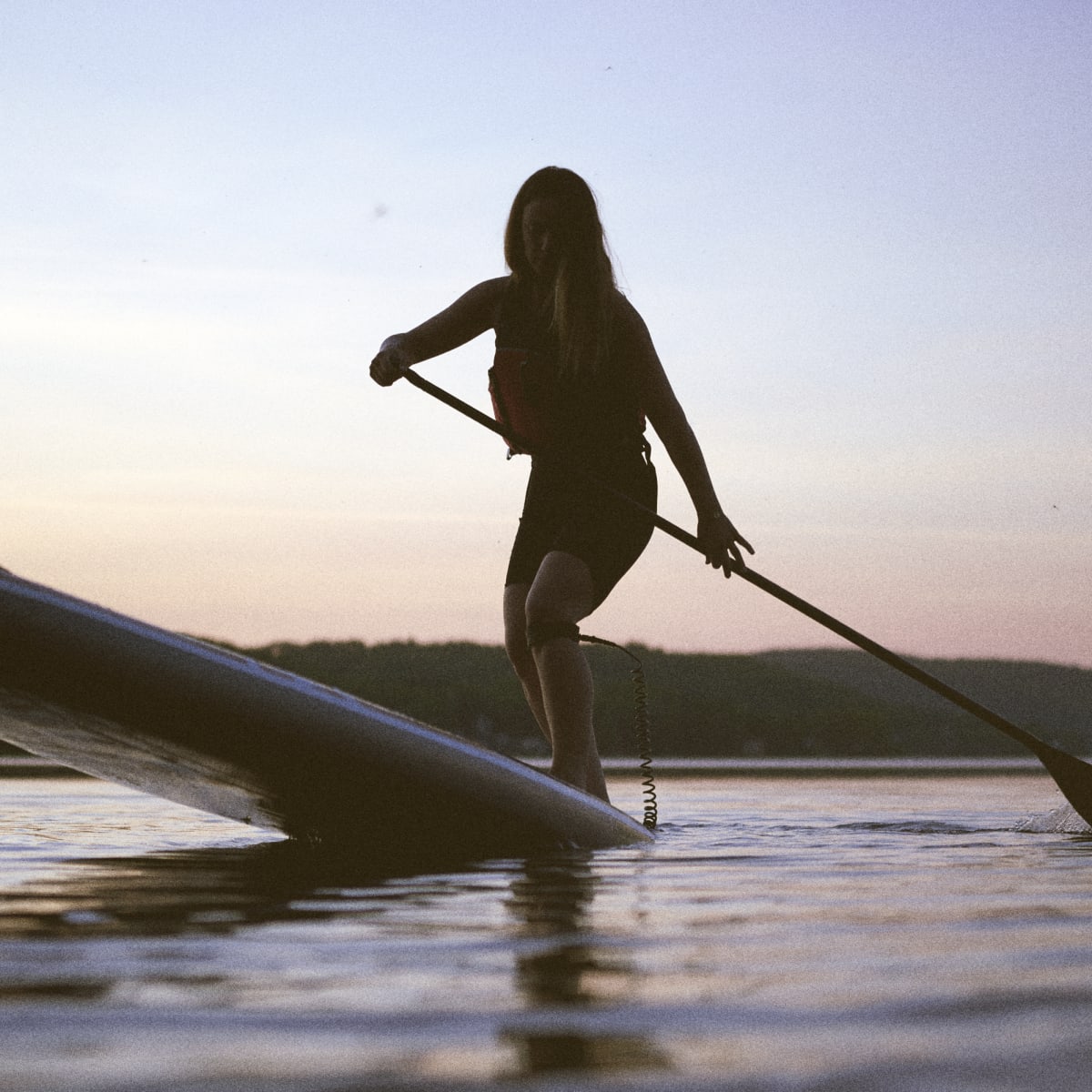 Femme en planche à pagaie le soir.