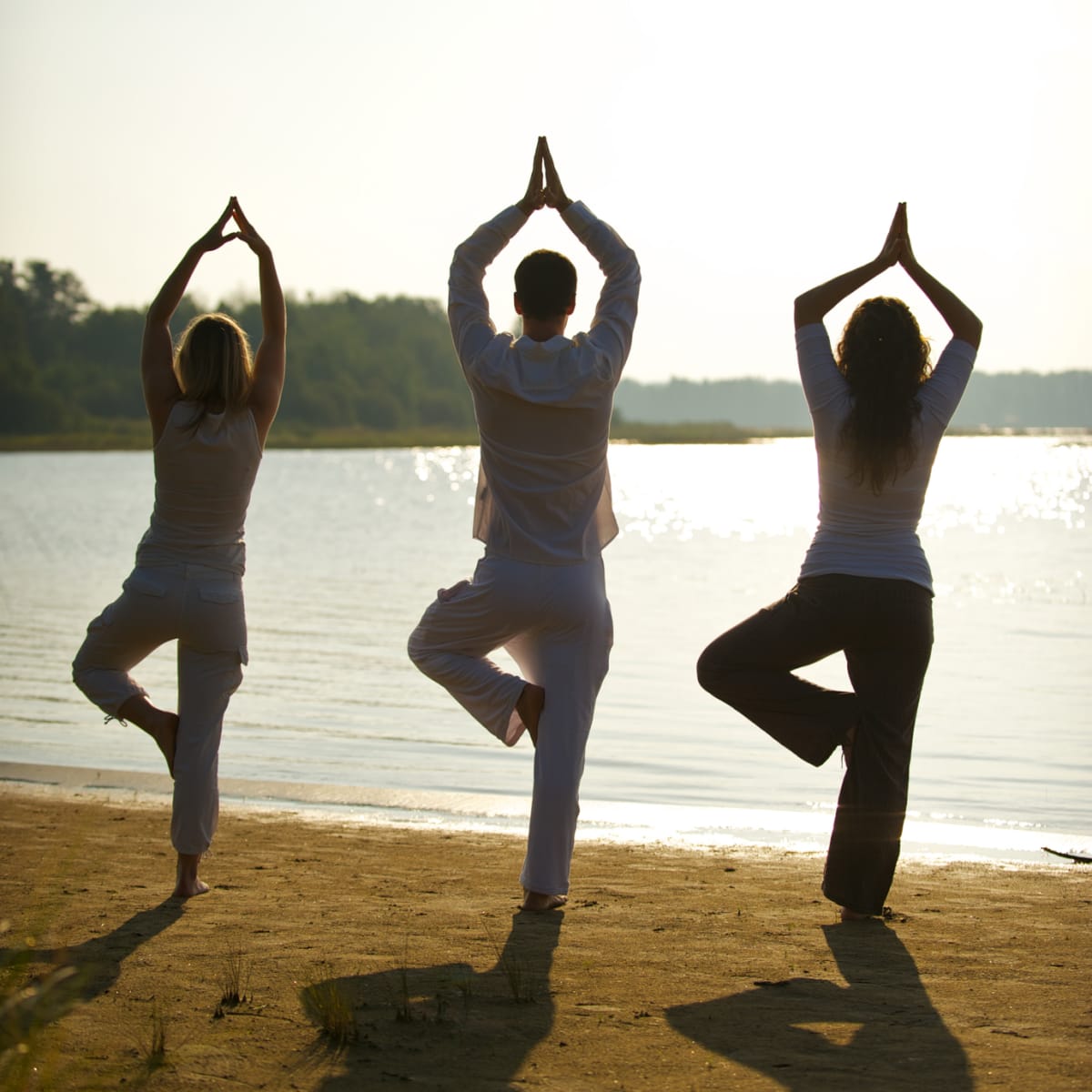 Trois personnes en train de faire du yoga sur la plage