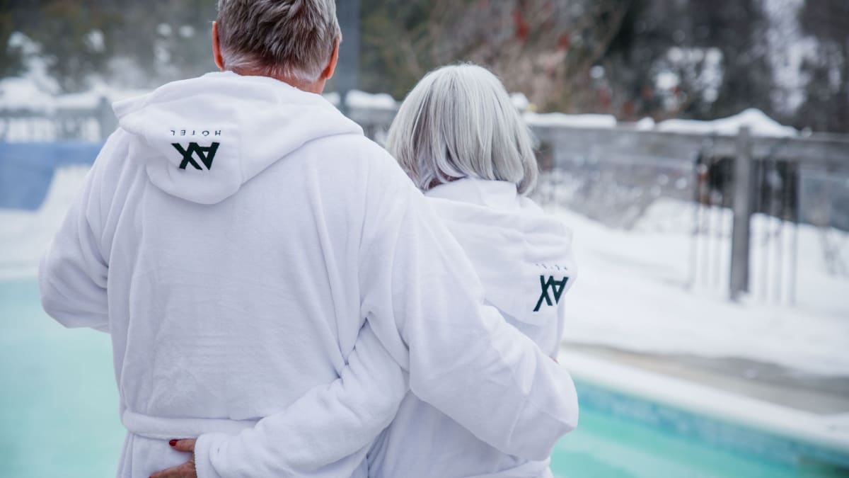 Un couple en peignoir s'enlace devant une piscine chauffée entourée de neige.