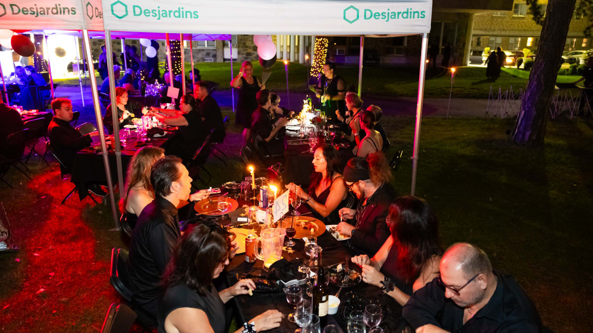 Groups of people dressed in black, seated at a long outdoor table