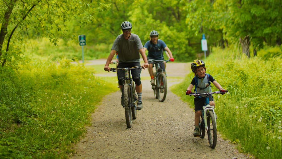 Family of 3 biking on a forest path.