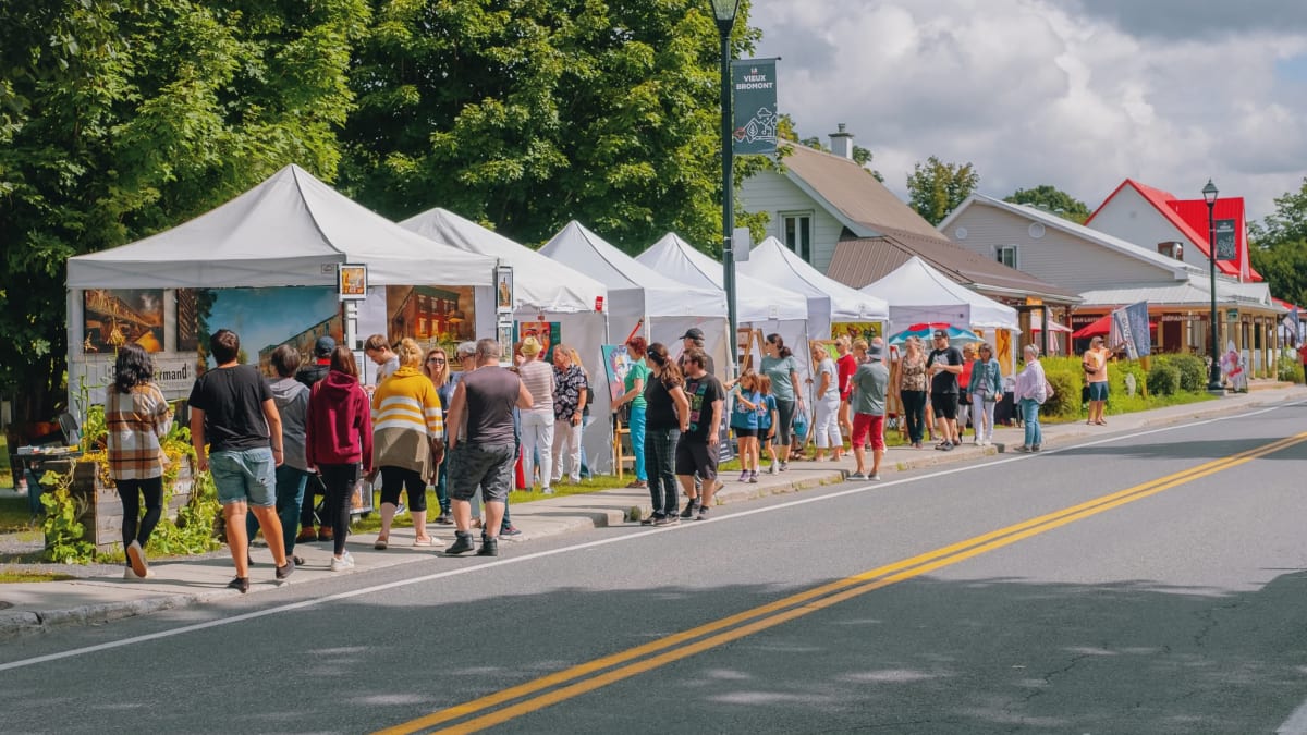 Rows of outdoor booths at the Bromont Art Symposium; many people are visiting each of the booths.