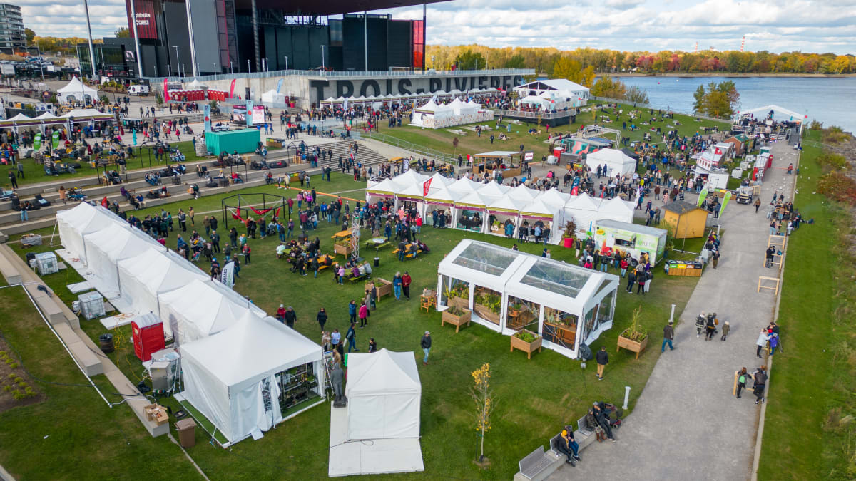 L'Amphithéatre Cogeco à Trois-Rivières au bord du fleuve avec des kiosques et spectateurs sur l'esplanade en gazon.