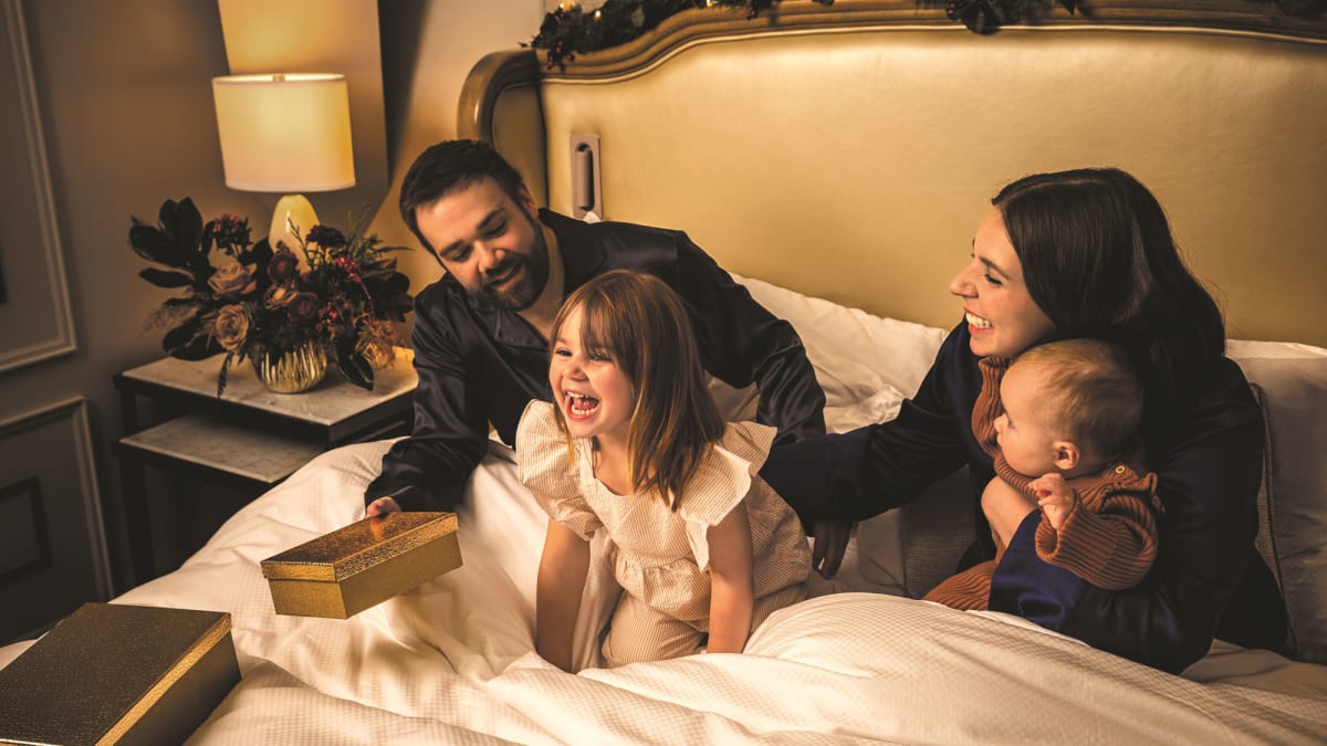 Deux parents avec une jeune fille et un bébé dans un lit d'hôtel aux allures luxueuses.