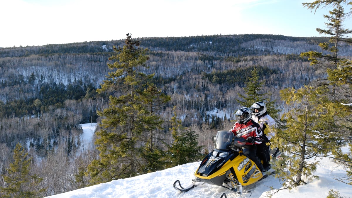 Deux personnes en motoneige devant les montagnes de la Mauricie