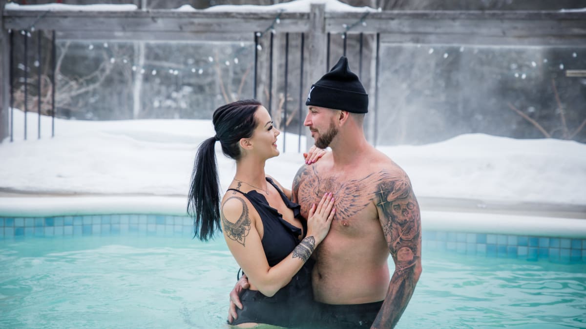 Jeune couple en maillots de bain dans la piscine extérieure l'hiver au AX Hôtel à Tremblant.
