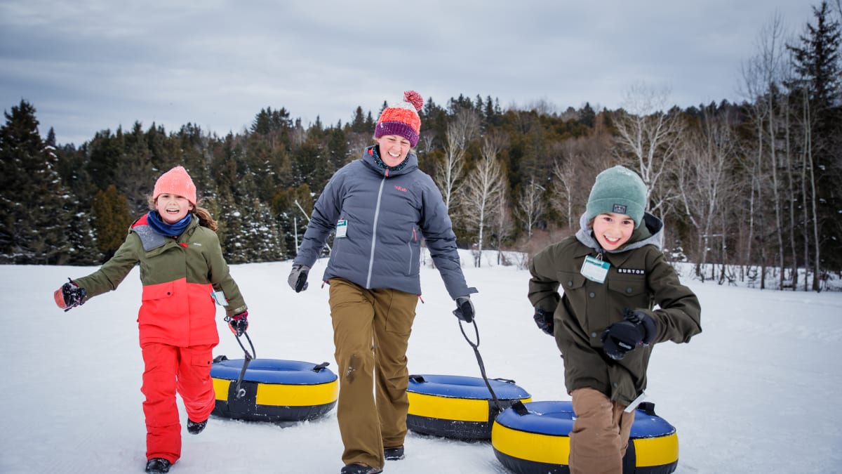 Une femme et deux enfants en habits de neige qui traînent des chambres à air pour la glissade