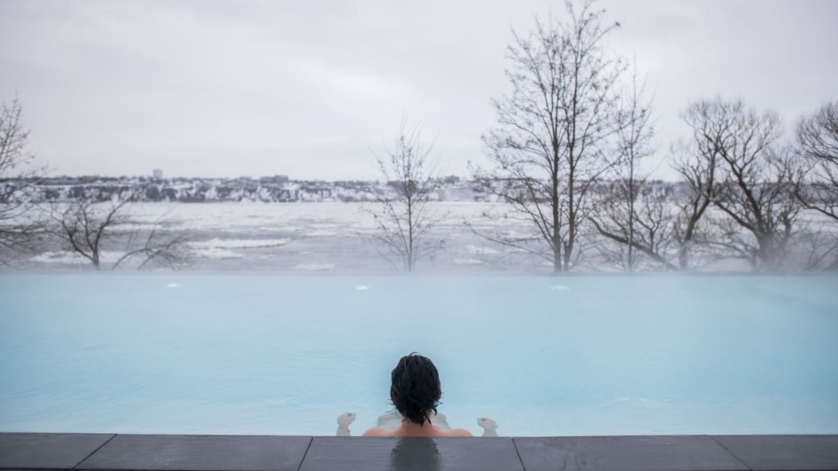 Vue de dos d'une personne dans un spa en train de regarder la vue sur le fleuve en hiver.