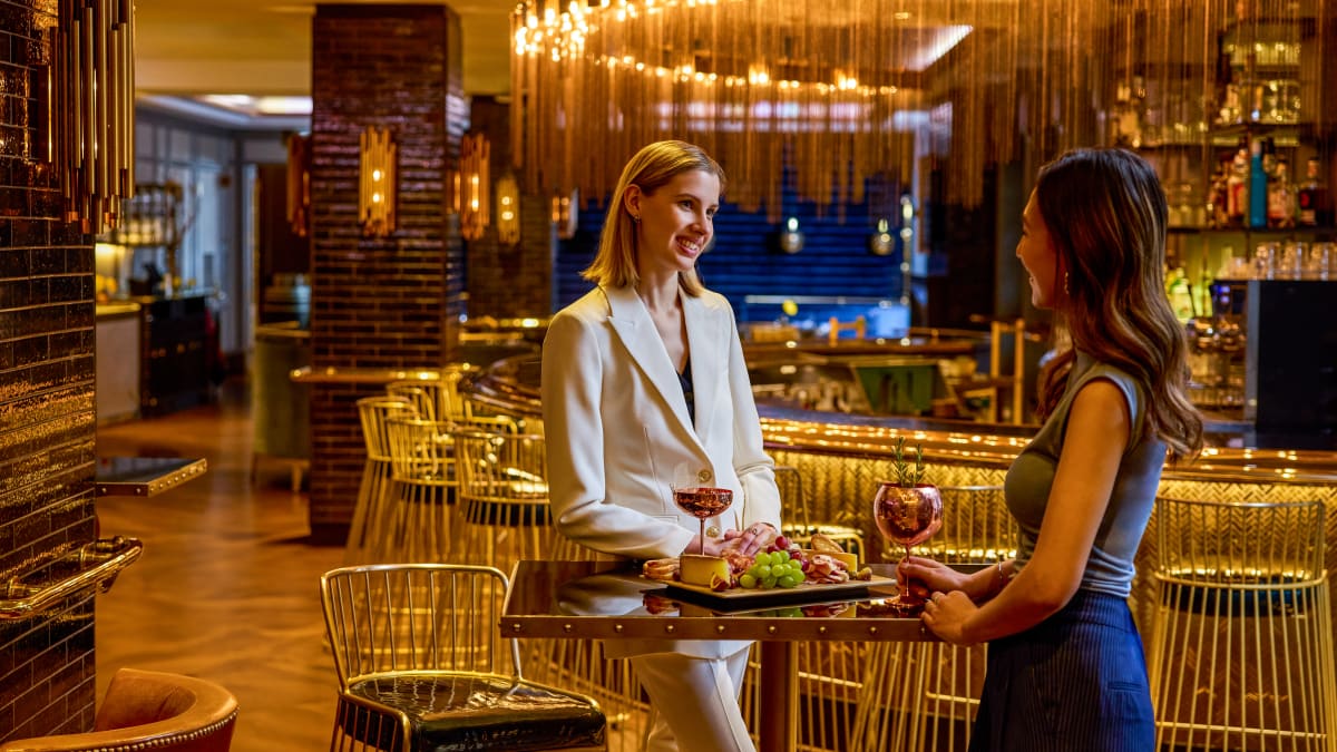 Two women enjoying a glass of red wine in a gold-accented dining venue.