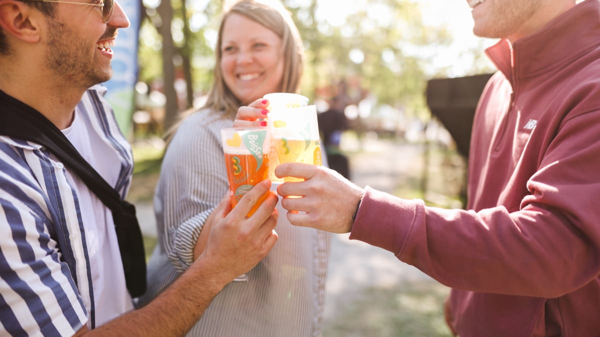 Three people making a toast with a glass of beer in hand.