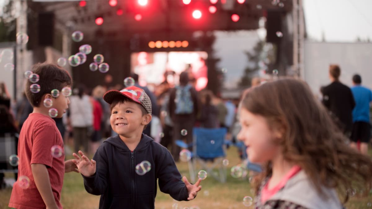 3 kids having fun in front of a stage at the festival.