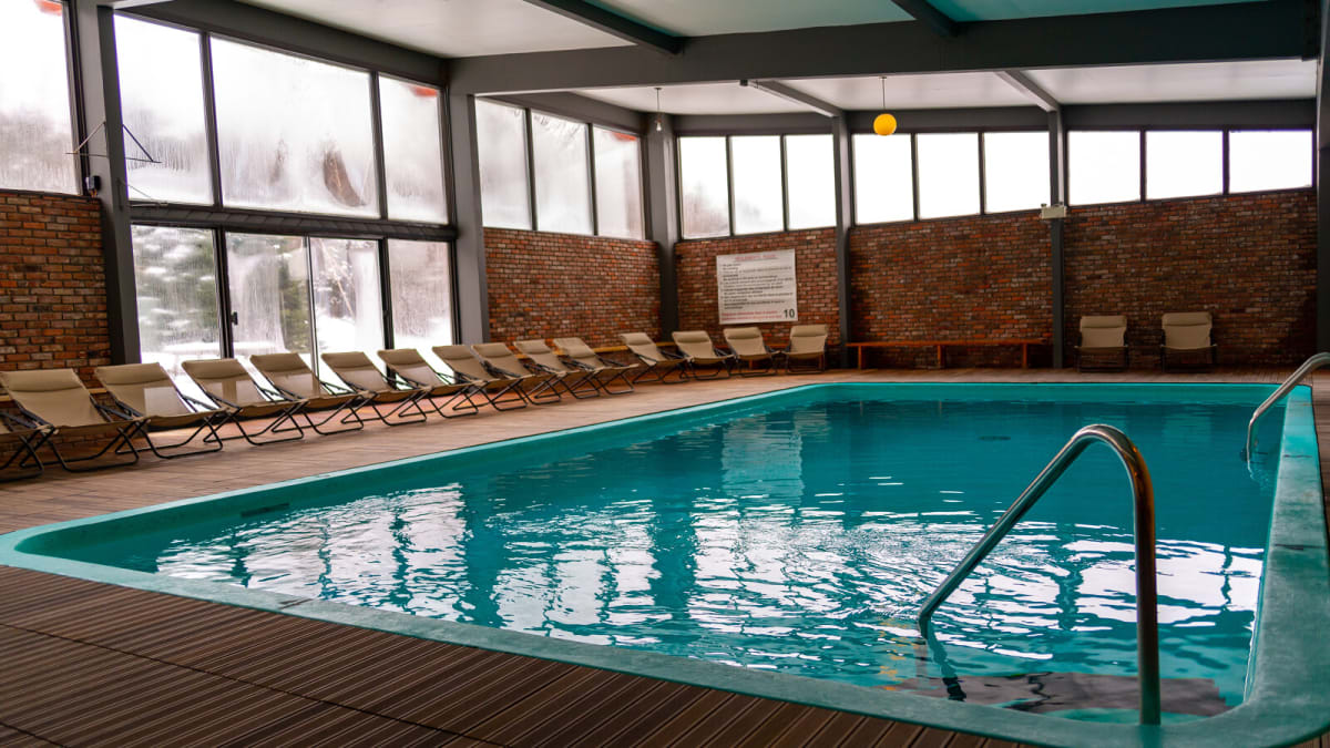 Indoor pool surrounded by chairs in a large room with windows.