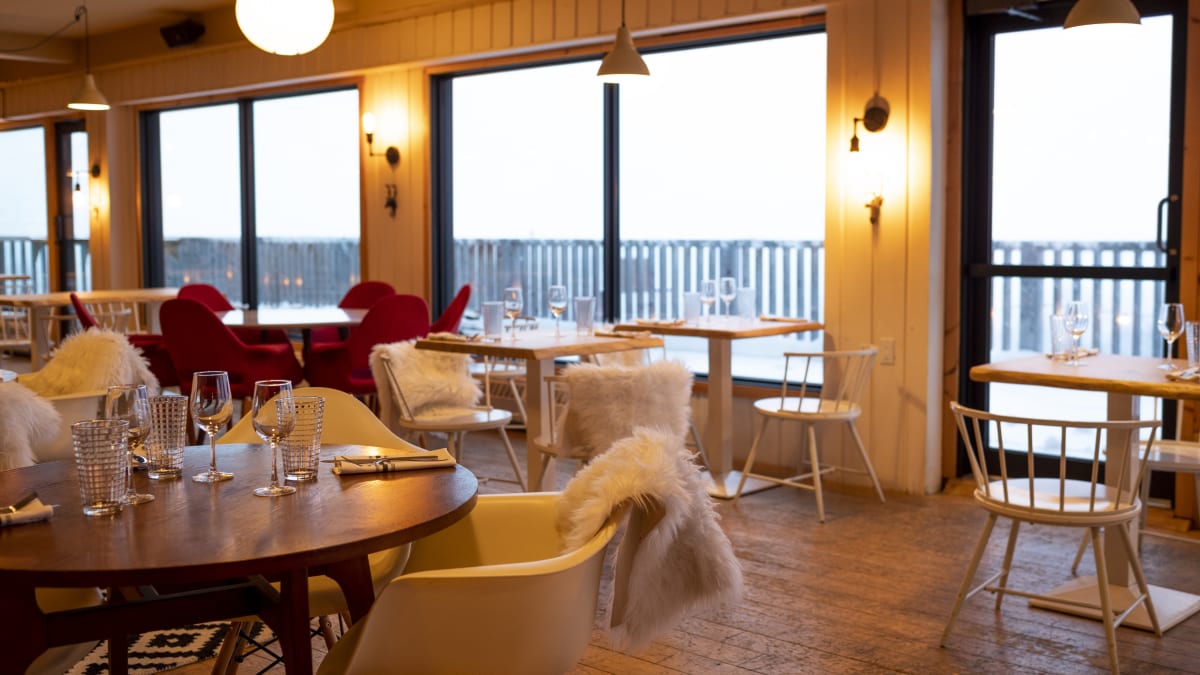 Inside of a cozy-looking bistro, with large windows and warm lighting