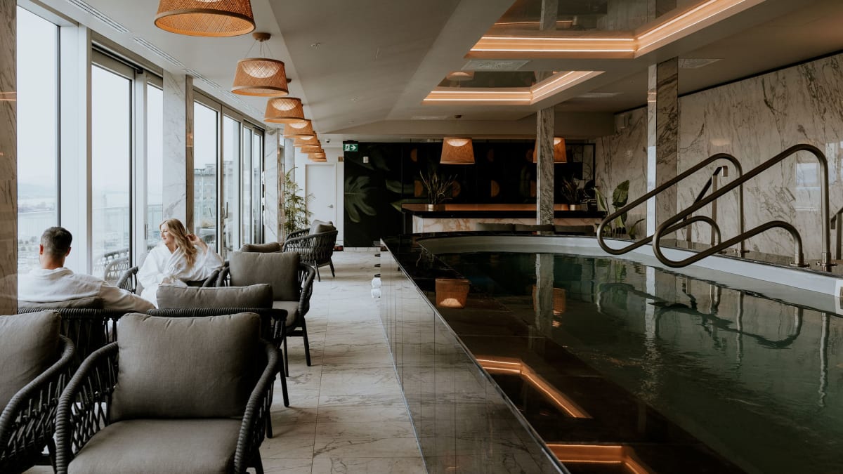 Deux personnes en peignoir assises près d’une piscine intérieure à l’ambiance zen; ils admirent la vue extérieure.
