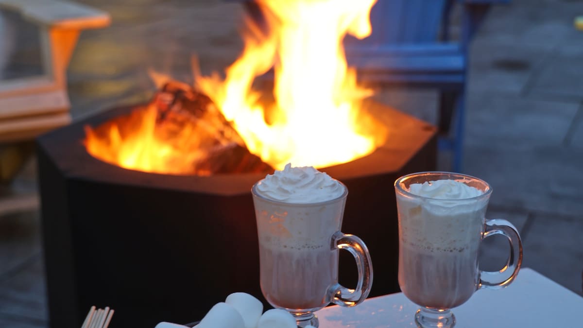 Outdoor firepit with two mugs of hot cocoa and ingredients to make s'mores.