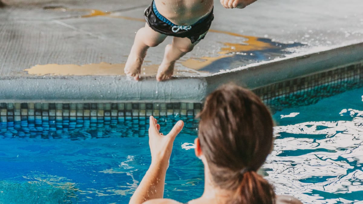 Mother in the hotel pool catching her son jumping in the water.