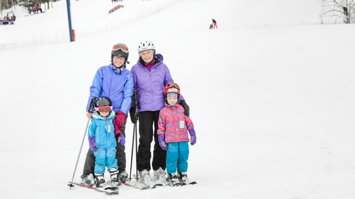 Mother, grandmother and two little girls in ski gear at the foot of the hill.