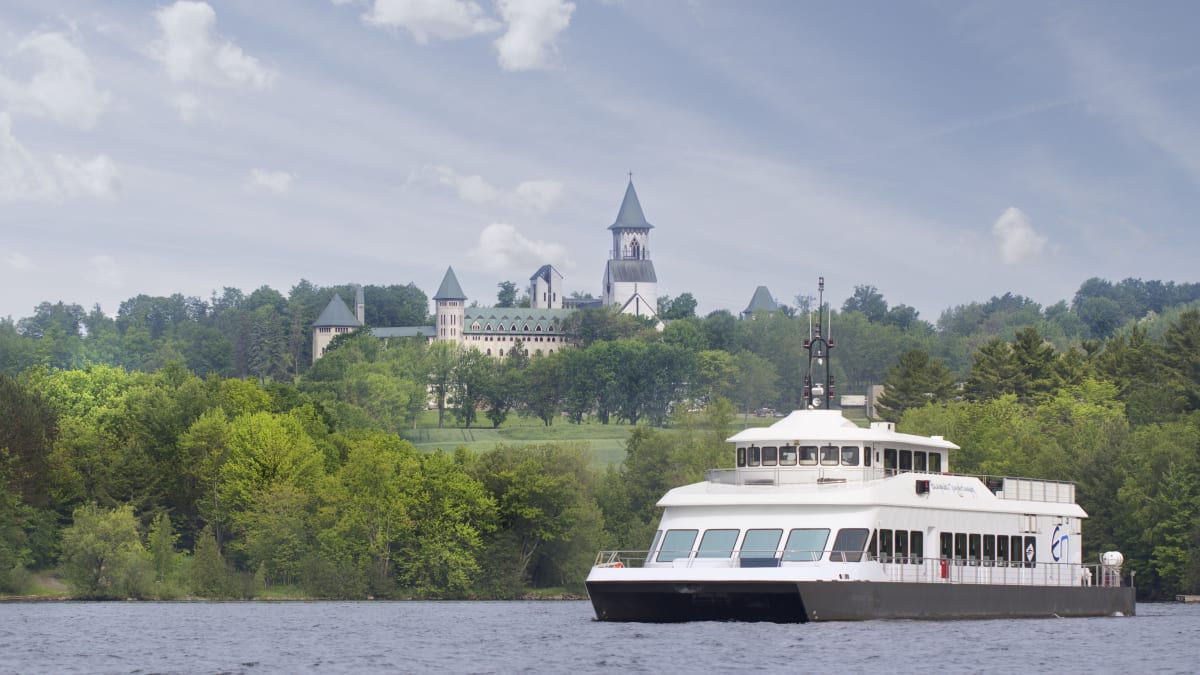 Navire de croisière sur un lac, avec une abbaye sur la rive en arrière-plan.