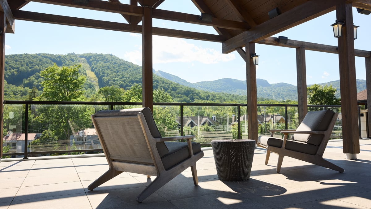 Une terrasse extérieure couverte, où se trouvent deux chaises confortables, donne sur un paysage montagneux.