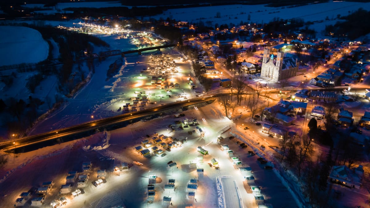 Village de pêche sur glace illuminé vu de haut dans la nuit.