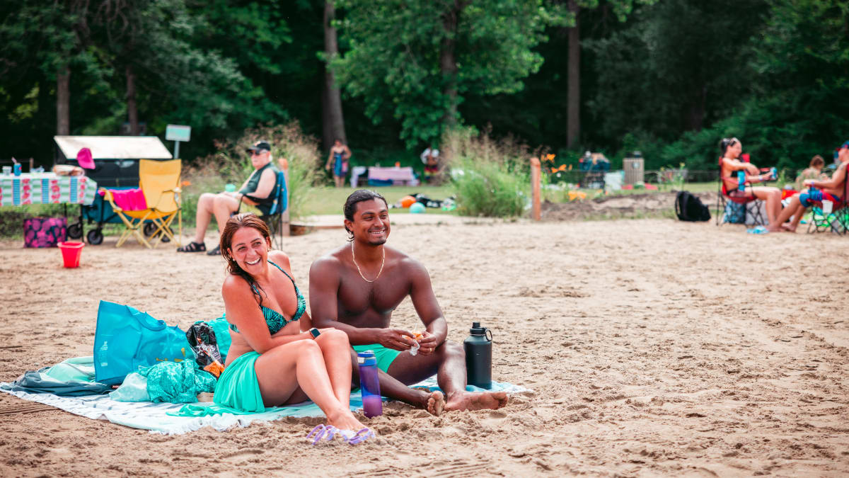 Couple aux visages heureux assis sur une serviette de plage.
