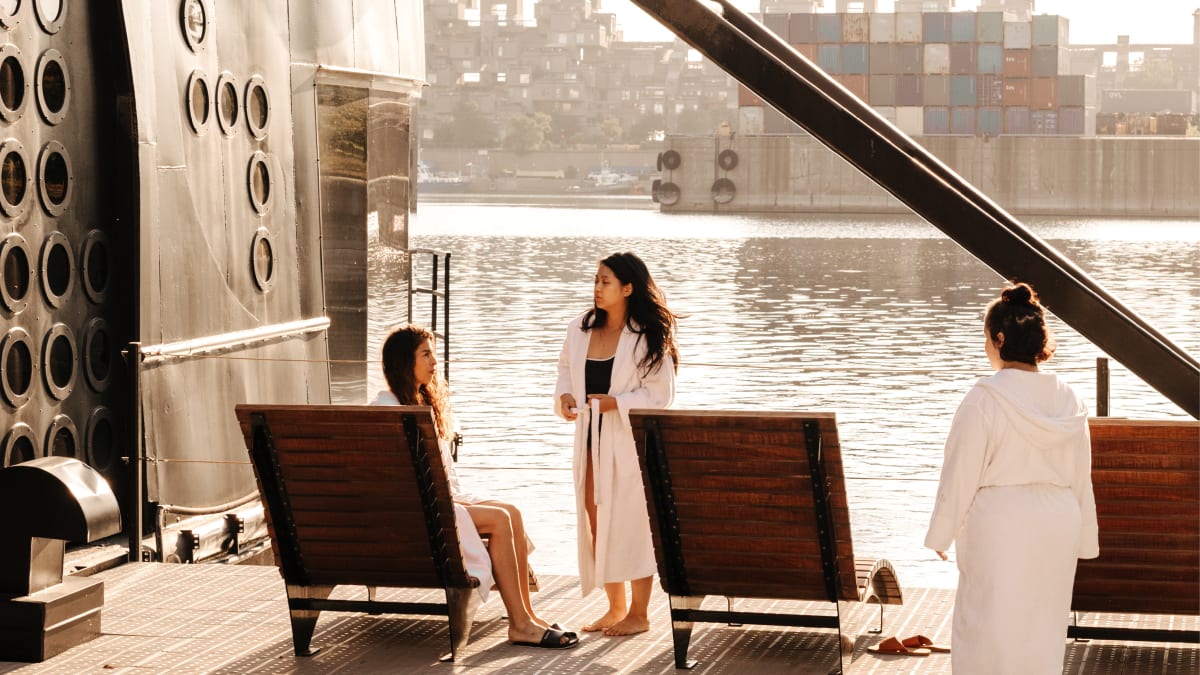 Trois femmes en peignoir sur la terrasse du spa, qui donne sur l'eau.