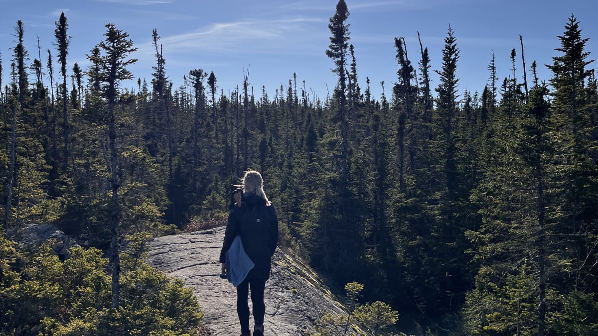 Woman on a trail at the top of a mountain under a bright sun.