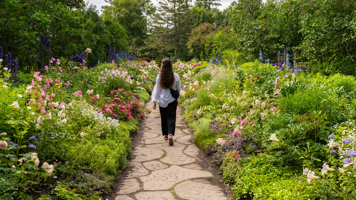 Femme qui marche qui traverse un jardin fleuri.