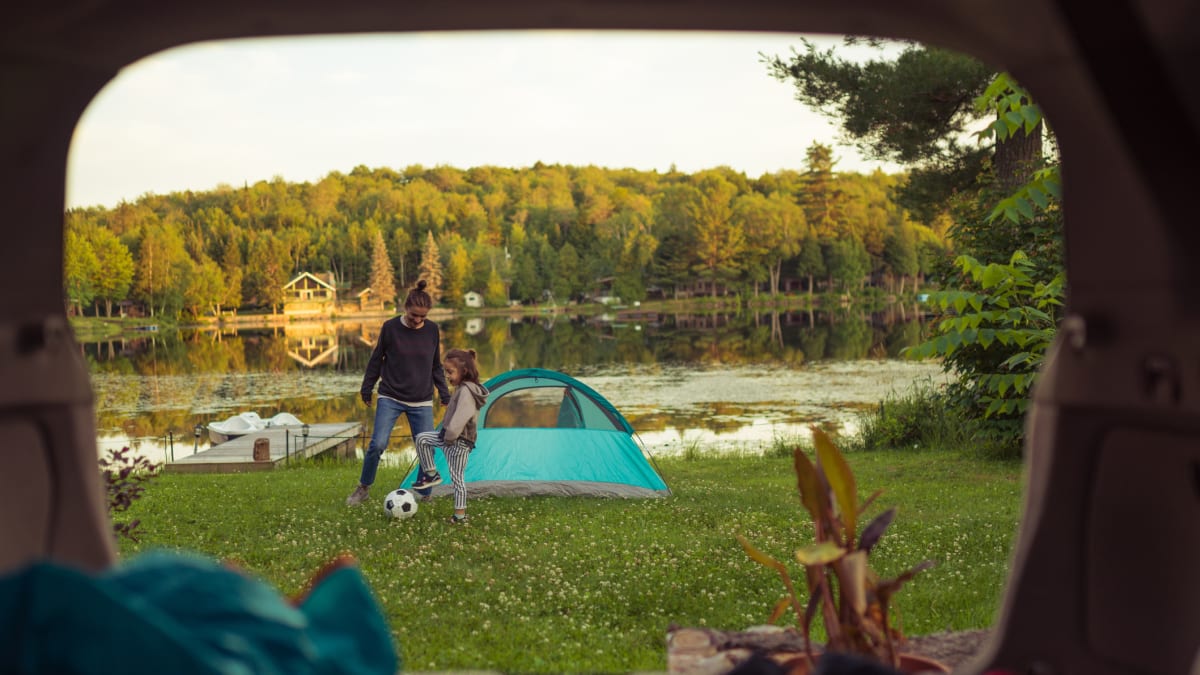 Une mère et sa fille en train de jouer au soccer à côté d’une tente au bord d’un lac.