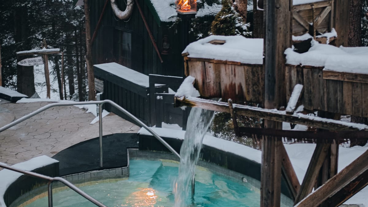 Un bain thermal entouré de neige et d’arbres à la tombée du soir.