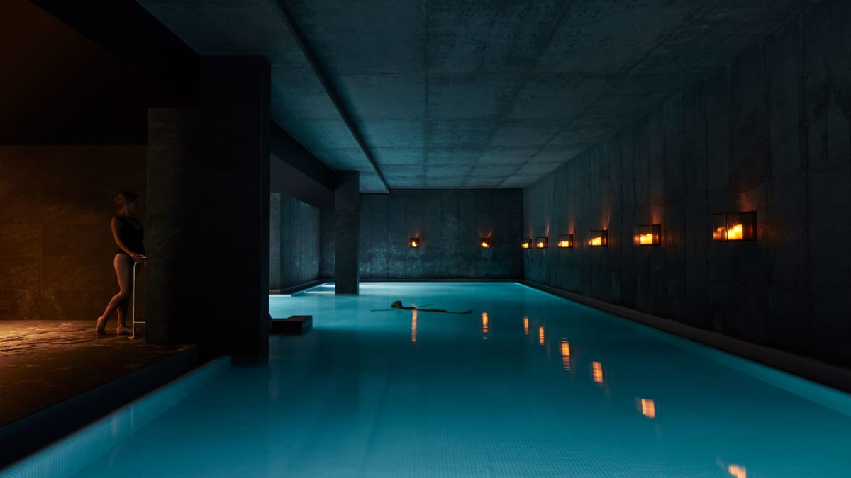 Indoor pool in a dark room lit only by soft lighting; a woman stands at the edge of the pool.