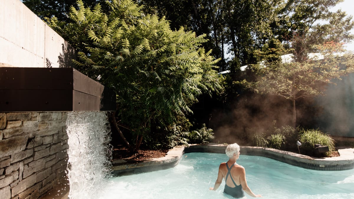 Woman in an outdoor thermal pool; a waterfall flows into the pool.