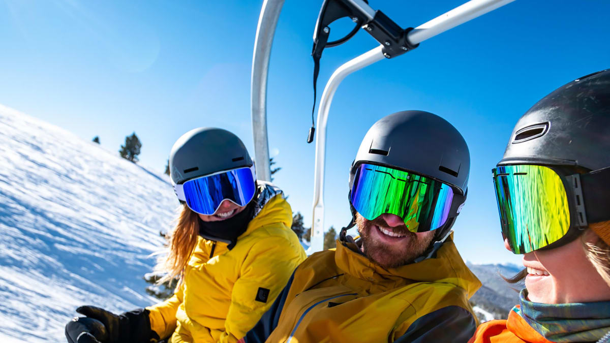 Three skiers in a lift, it's a sunny day and they're smiling.
