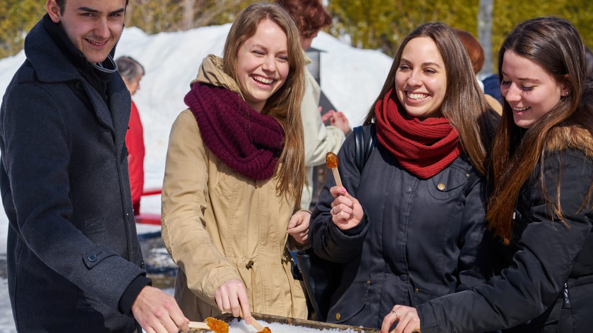 A man and three women all smiling as they enjoy taffy on snow.