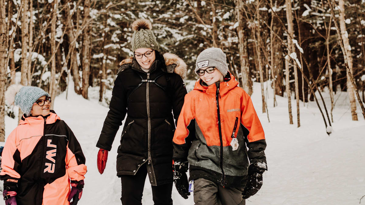 Une mère et deux enfants, tous souriants, dans une forêt enneigée.