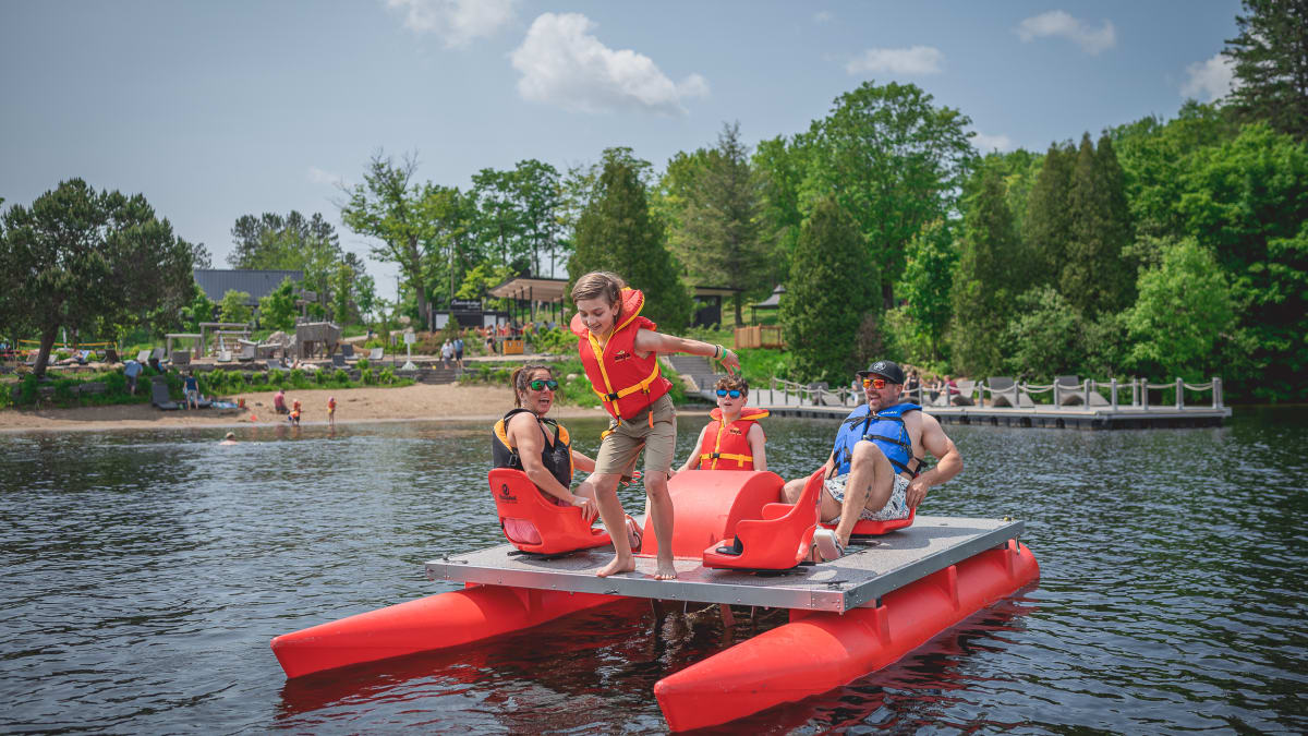 Family of four on a big pedal boat; a boy is about to jump into the lake.