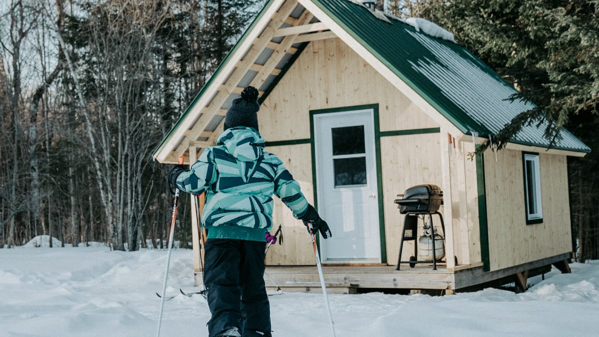 Child wearing skis returning to a cabin.
