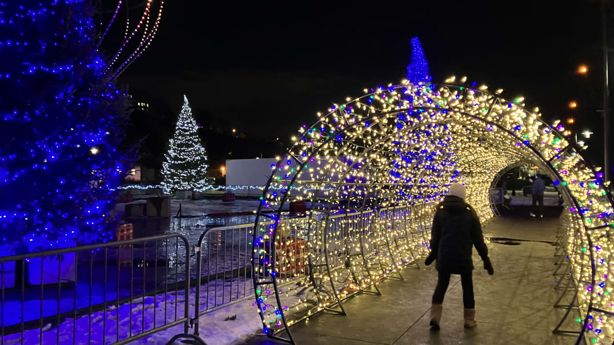 Woman walking under an illuminated arch outside.