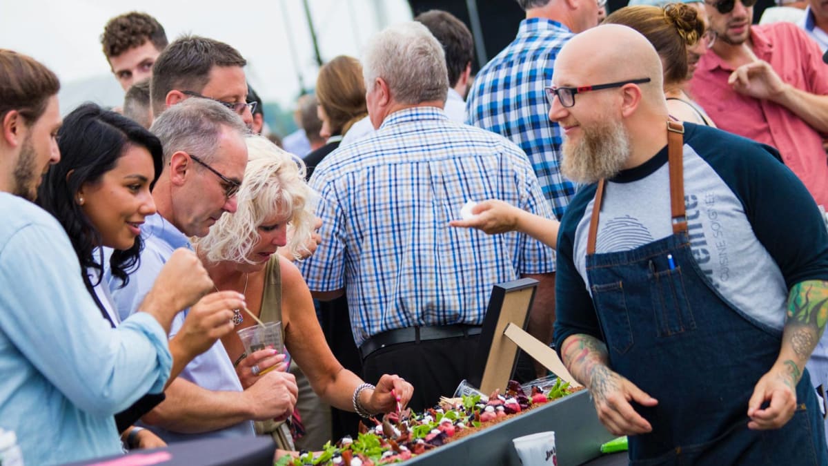 Culinary exhibitor and tasters sampling appetizers with the crowd in the background.