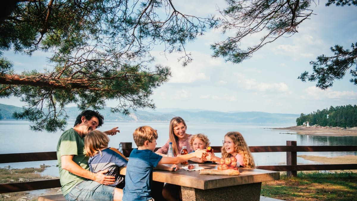 Famille avec jeunes enfants assis autour d'une table de pique-nique à côté du Fjord du Saguenay