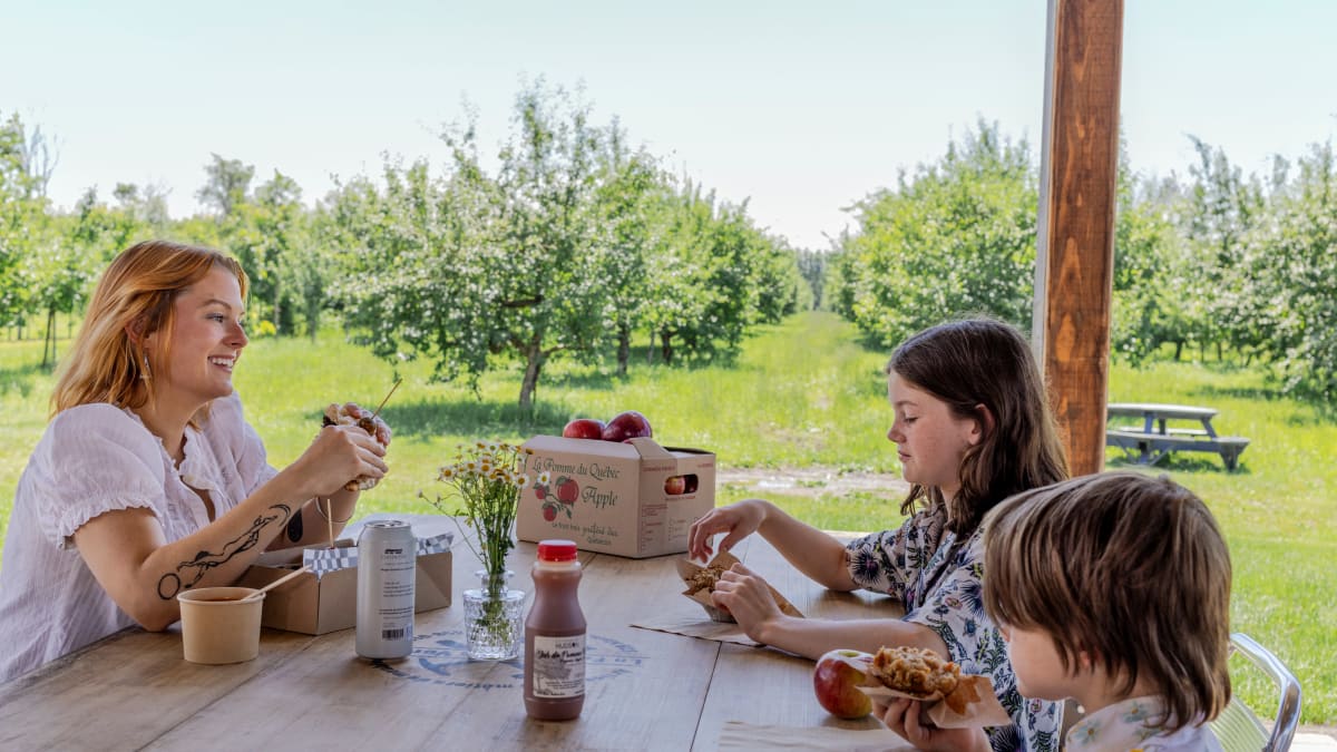 A mother and her two children enjoying apple products in an orchard.